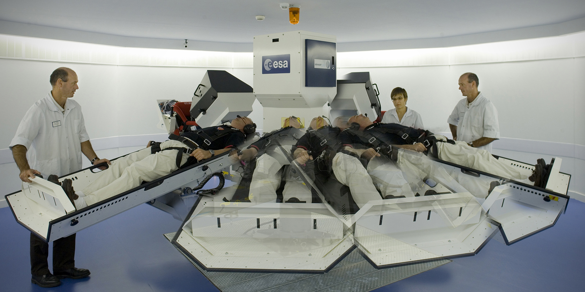 Une personne allongée dans une centrifugeuse qui tourne sous la surveillance de deux médecins