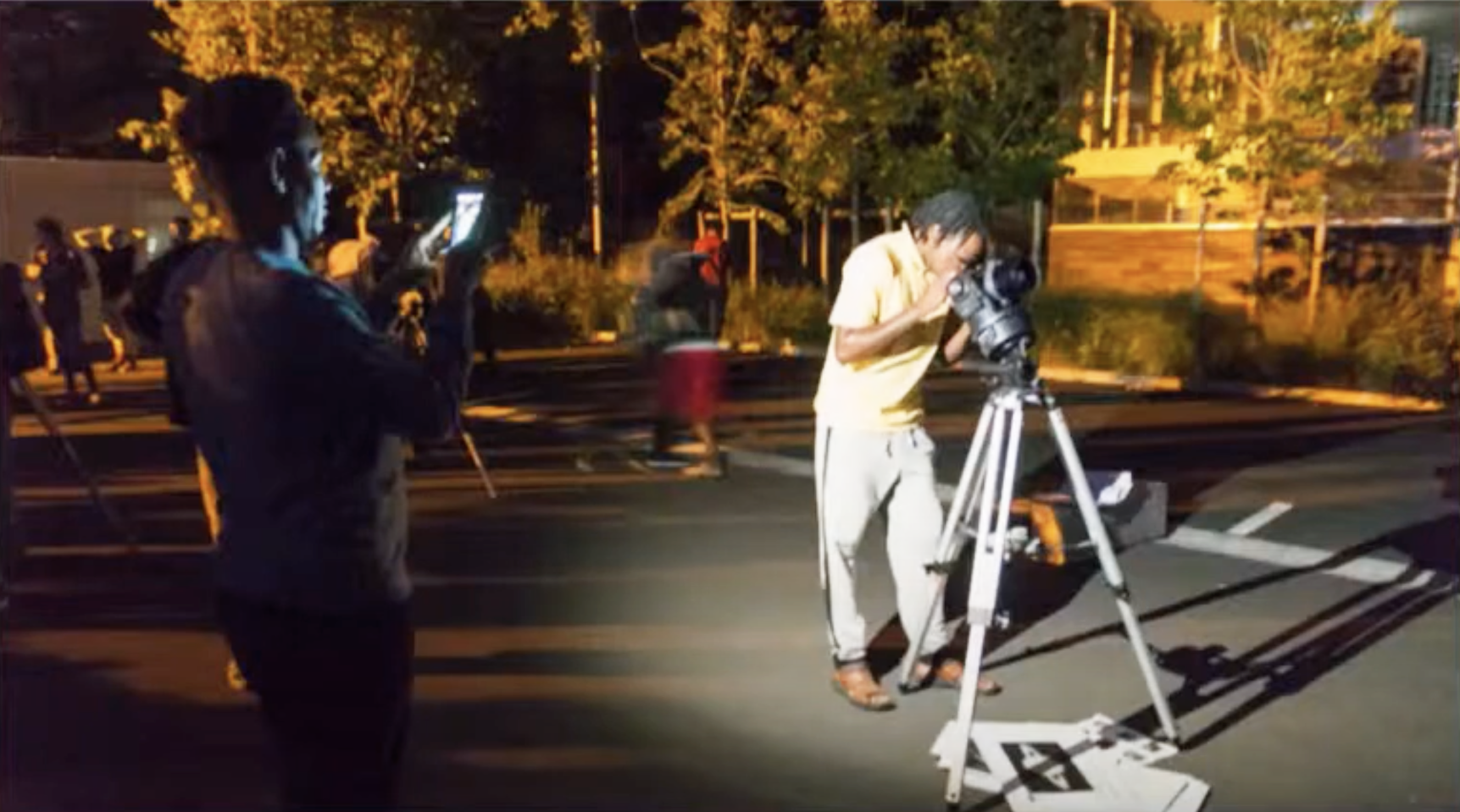 Un migrant observant dans un télescope sur un parking pendant qu'un autre le prend en photo