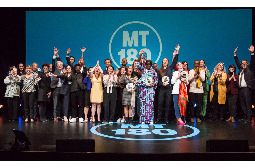 Participants souriants sur une scène avec le logo MT180
