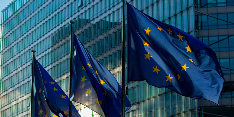 Les drapeaux de l'Europe flottent au vent devant un bâtiment en verre