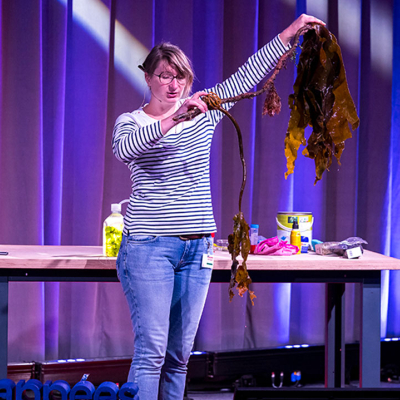 Une chercheuse sur la scène de la Cité des sciences montre une algue au public